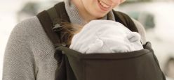 Mother smiling down at a baby in a carrier cover by a fleece cover.